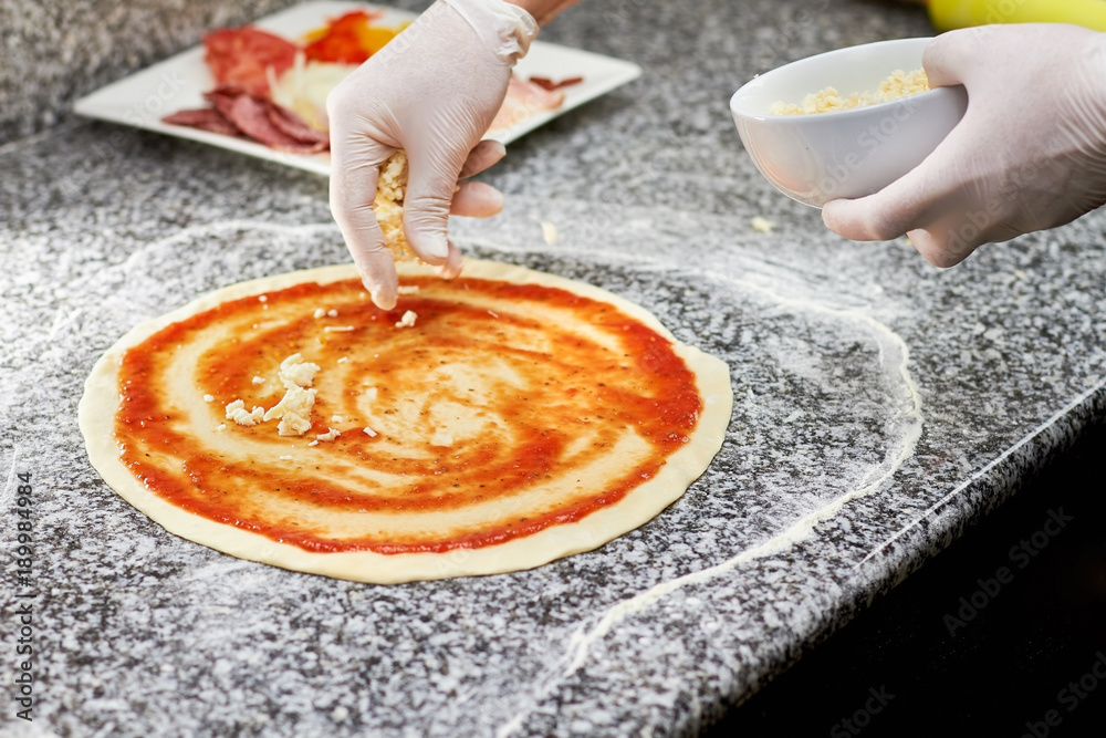 Sprinkling cheese on pizza crust. Process of cooking pizza, adding cheese. Scattering cheese on pizza.