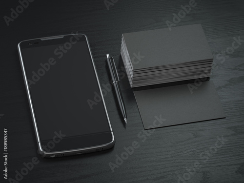Mockup of black blank business cards, black mobile phone and pen on the black wooden desk background.
