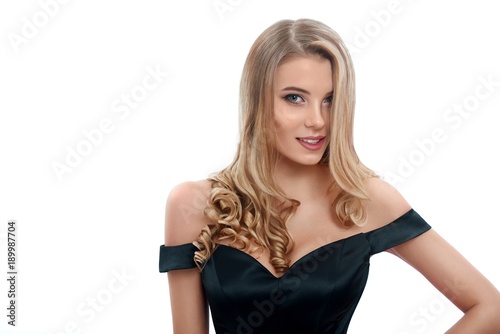 Portrait of a beatiful girl with blonde curly hair in a nice evening dress with a open top. Photo was made on the white studio background.