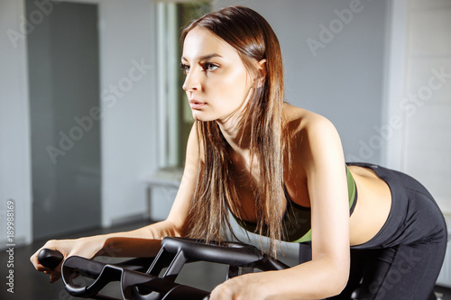 Young woman working out on the exercise bike at the gym, intense cardio workout.