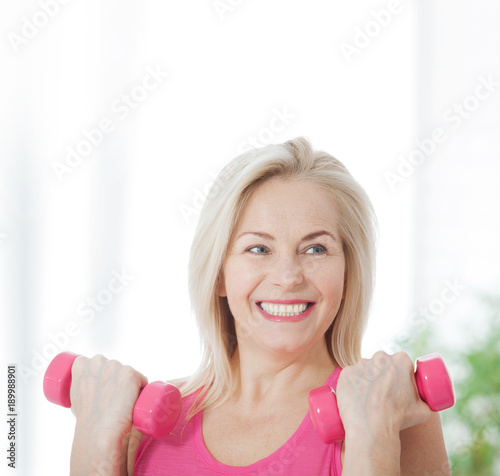 Happy middle aged woman lifting dumbbells at home in the living room