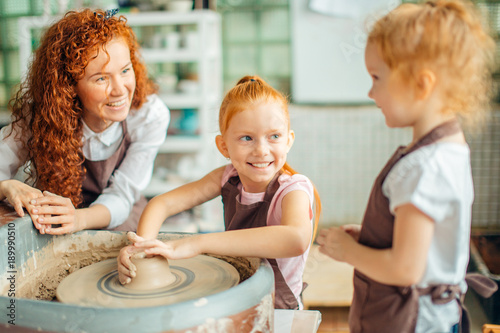 young mother and two redhead daughters made clay cup with pottery wheel photo