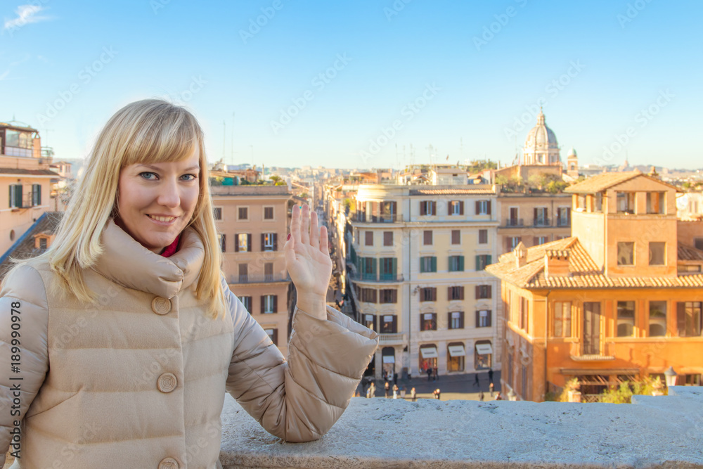 Portrait of a happy young blond woman waving her hand against the background of Rome Italy.