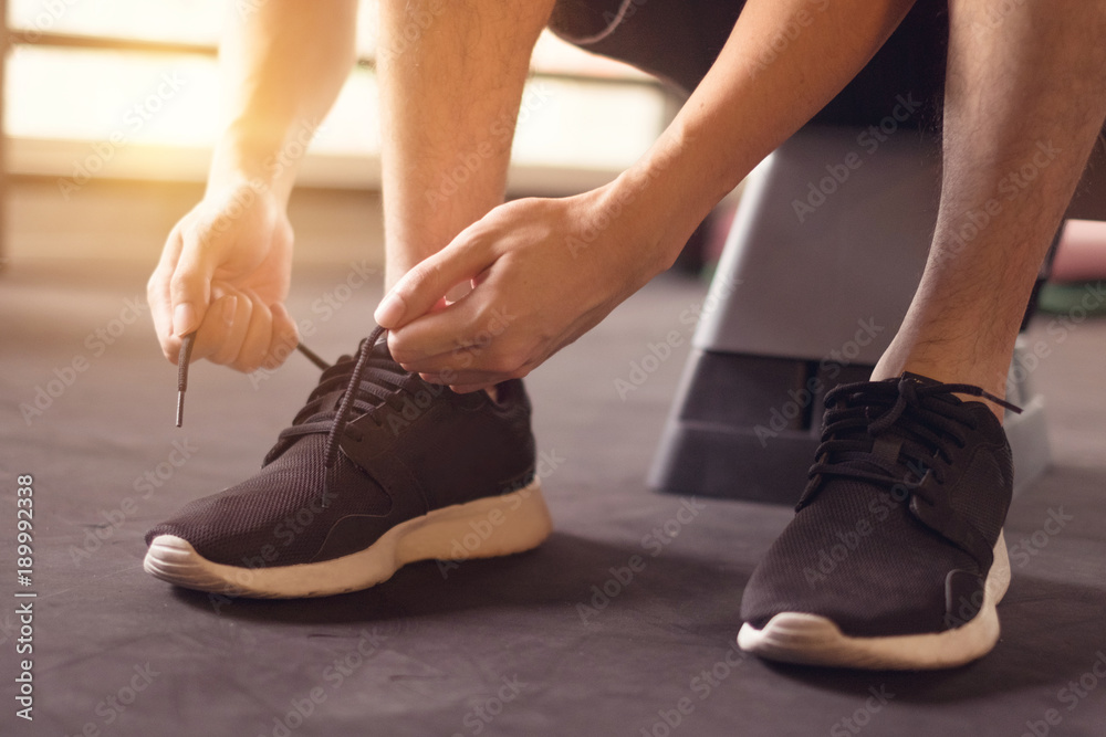 Man tying running shoes on black floor background in gym.