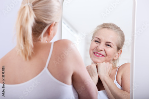 Middle aged woman looking at wrinkles in mirror. Plastic surgery and collagen injections. Makeup. Macro face. Selective focus