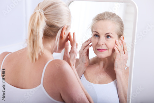 Middle aged woman looking at wrinkles in mirror. Plastic surgery and collagen injections. Makeup. Macro face. Selective focus