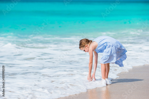 Adorable little girl in the shallow water. Beautiful kid washing her hands in the wave