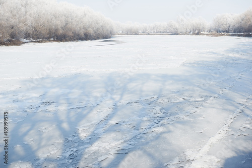 frozen river in winter forest, beautiful wild landscape with silhouettes of the trees on ice
