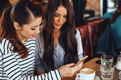 Two young women looking in smartphone screen in cafe