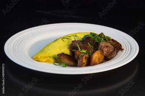 French omelet with crispy home fries and green onions on a white plate.
