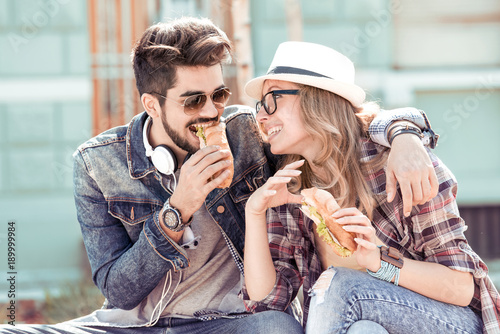 Couple eating sandwich and talking outdoor.