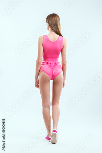 Fototapeta Naklejka Na Ścianę i Meble -  Rear view of beautiful young girl in pink swimsuit and sneakers posing in studio