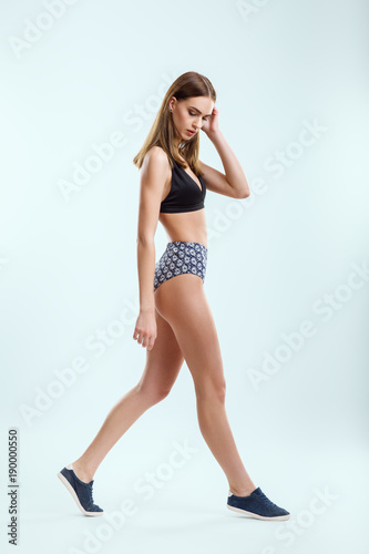 Walking beautiful young girl in swimsuit and sneakers in studio