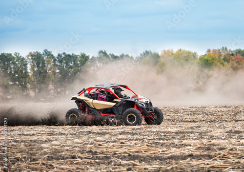 Quad bike with two pilots in thick dust rides on plowed field