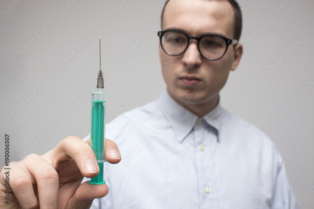 Young handsome doctor holding and looking at small syringe. Healthcare and medicine concept. Selective focus and shallow DOF Young handsome doctor holding and looking at small syringe. Healthcare and medicine concept. Selective focus and shallow DOF