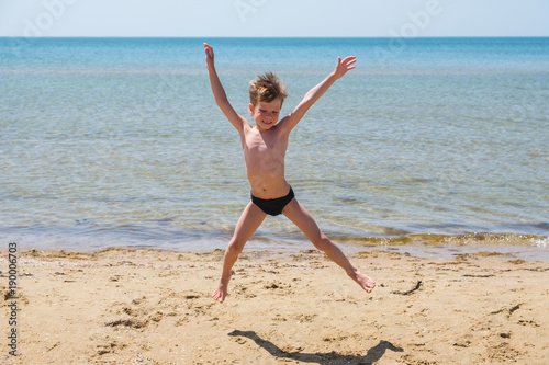 Vászonkép Six-year-old boy in black speedo jumping into the sea and smiles.