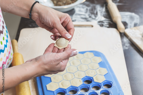 The process of making delicious homemade dumplings. Female hands hold freshly dumplings on the background of kitchen workspace