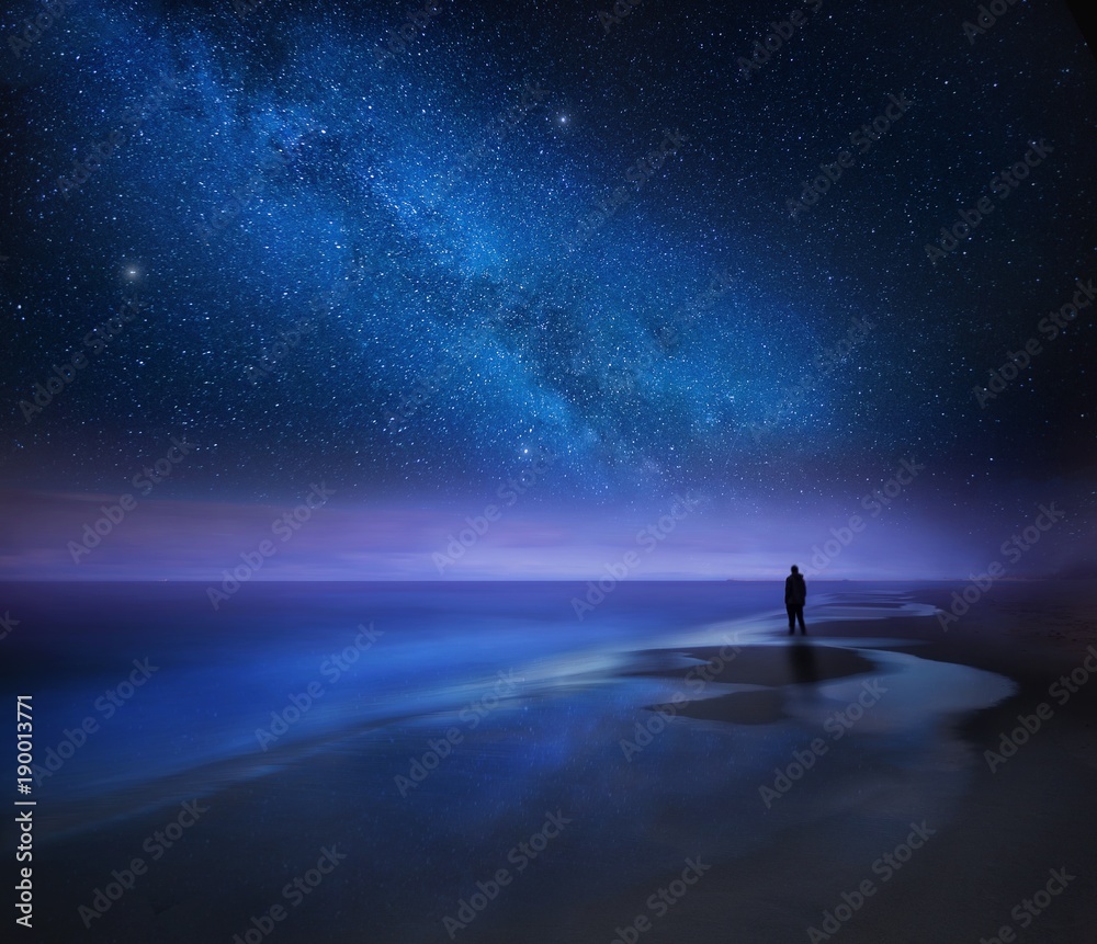 Starry night sky over sea and beach with man silhouette
