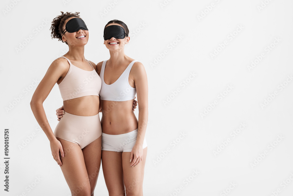 Portrait of slim women wearing tight underwear and black sleep masks. They  are hugging and smiling. Copy space in right side. Isolated on background  Stock-foto