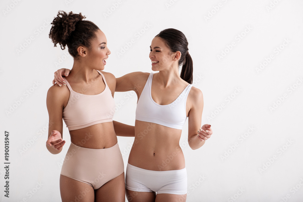 Foto de Happy athletic friends hugging each other and smiling. Girls are  wearing tight underwear. Isolated on background do Stock