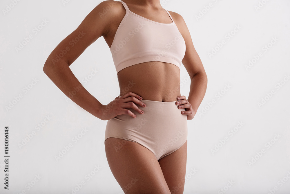 Fitness as a lifestyle. Close up of fit female body standing in comfortable lingerie. Isolated on background - obrazy, fototapety, plakaty 