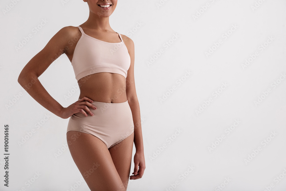 Health concept. Smiling african woman taking care of her slim figure. She is wearing comfortable underclothes. Copy space in right side and Isolated on background - obrazy, fototapety, plakaty 