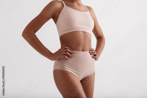 Fitness as a lifestyle. Close up of fit female body standing in comfortable lingerie. Isolated on background