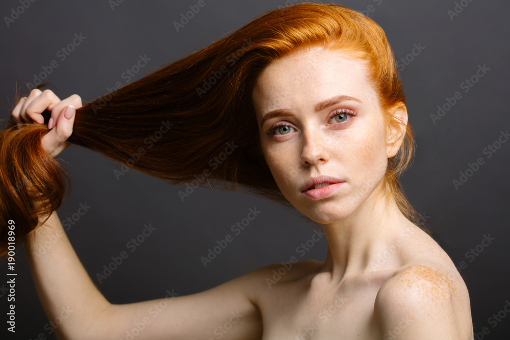 Valokuva beautiful redhead woman holding her healthy and shiny hair, studio gery