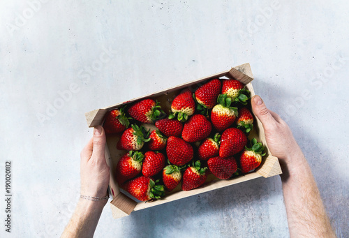 men's hands hold a wooden box with Pile of juicy ripe organic strawberries . sale on the market