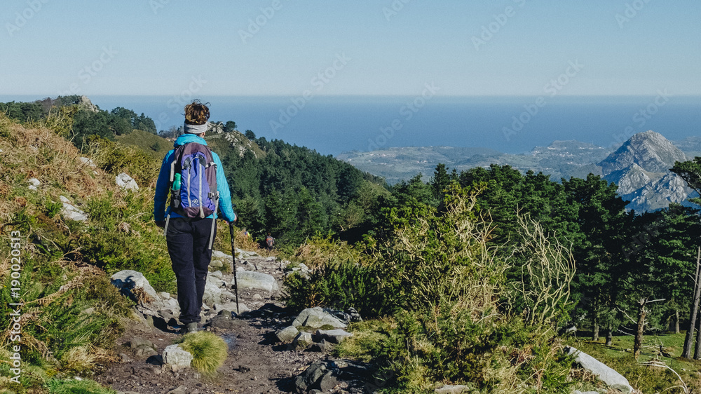 A woman hiking through the mountains with a green landscape and the sea in the background