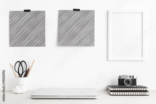 Modern and stylish workspace with laptop computer closed, empty phoro frames, posters office supplies, camera at home or studio. Mock up. photo