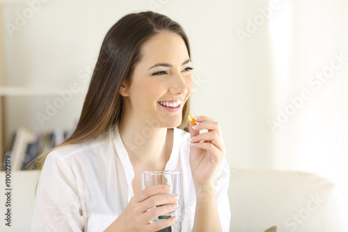 Happy woman taking a vitamin yellow pill at home