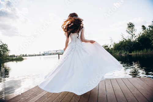 Billede på lærred Redhead bride in a beautiful wedding dress on a wooden bridge on a lake