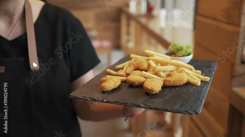 Chef is bringing out food to the customer. Chicken nuggets with french fries in slow motion. Served with tomato sauce and lettuce salad leaf. Delicious food being served.