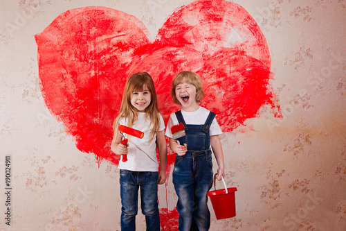 a boy and a girl with a roller in jeans and a white T-shirt, a brush and a bucket paint the wall in red.