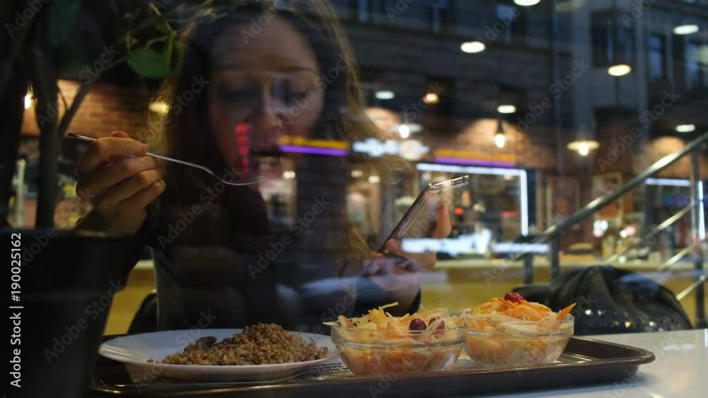 Girl eats at the cafe and and chatting in the phone, view through window, 4k. Girl eats at the cafe and and chatting in the phone, view through window, 4k.