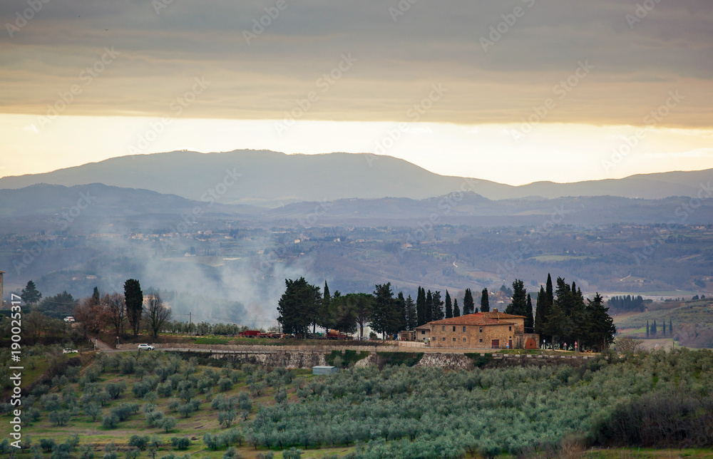 Tuscan landscape with cypress, trees and ancient buildings.