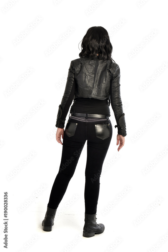 full length portrait of black haired girl wearing leather outfit. standing pose view from behind, on a white background full length portrait of black haired girl wearing leather outfit. standing pose view from behind, on a white background