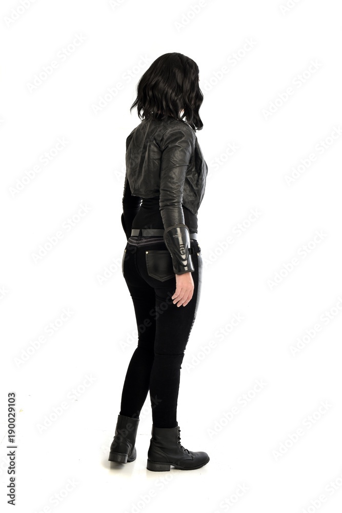 full length portrait of black haired girl wearing leather outfit. standing pose view from behind, on a white background full length portrait of black haired girl wearing leather outfit. standing pose view from behind, on a white background