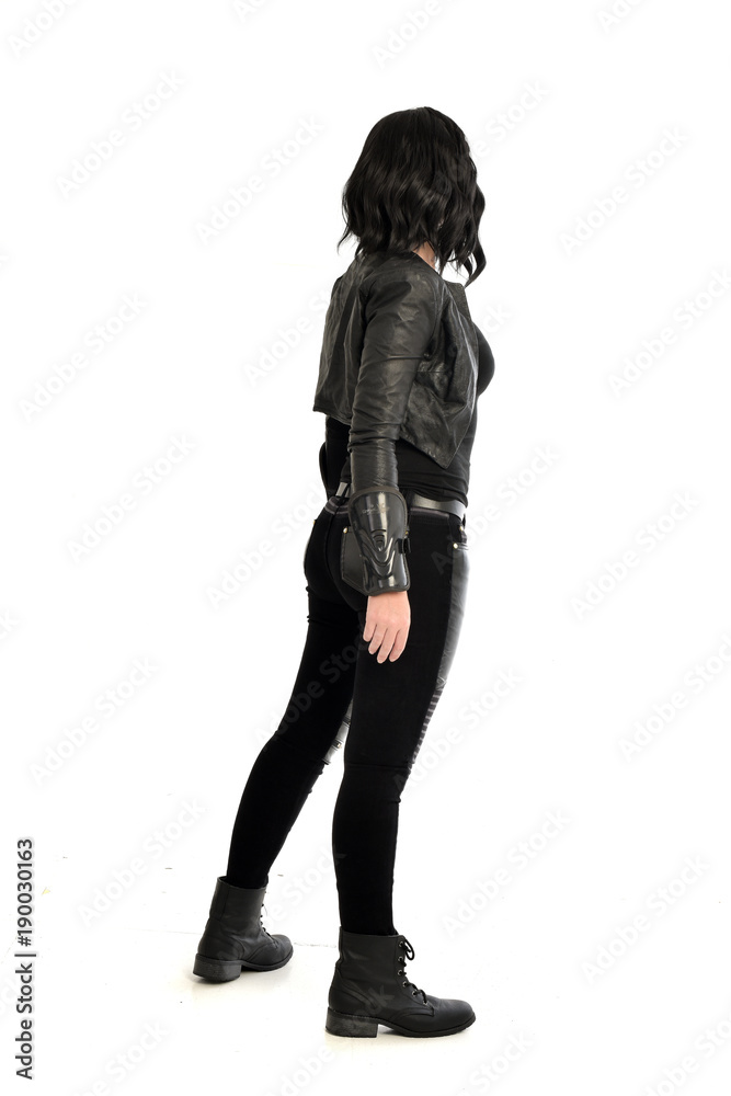 full length portrait of black haired girl wearing leather outfit. standing pose view from behind, on a white background full length portrait of black haired girl wearing leather outfit. standing pose view from behind, on a white background