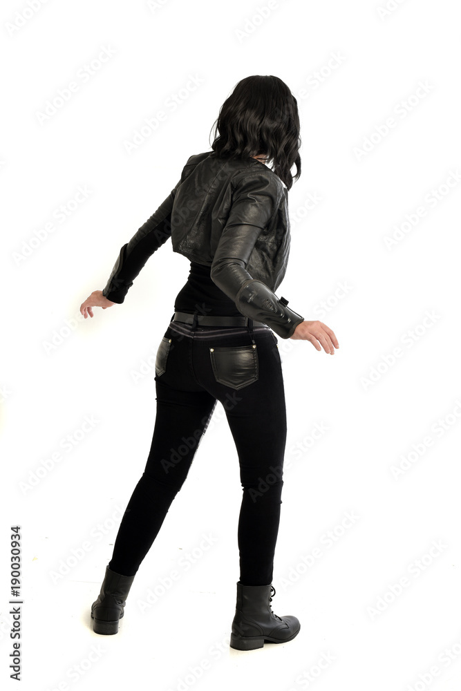 full length portrait of black haired girl wearing leather outfit. standing pose  view from behind, on a white background