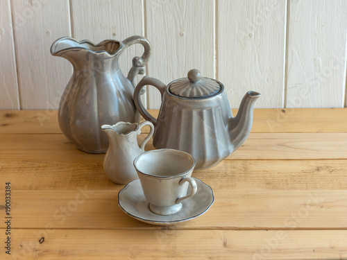 Tea set is Gray on a wooden background. Teapot, creamer, Cup and saucer on the table. Ceramic kitchenware