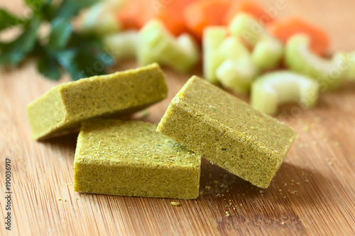 Vegetable bouillon, stock or broth cubes on wooden board, photographed with natural light (Selective Focus, Focus on the upper edge of the two cubes in the front)