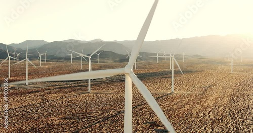 Aerial reveal of windmill in wind farm in desert at sunset 
