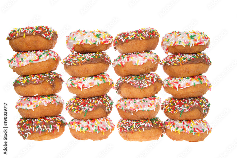Cake donuts frosted with chocolate and vanilla frosting, rainbow candy sprinkles, stacked in rows, alternating chocolate and vanilla frosted isolated on white background