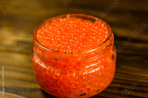 Red caviar in glass jar on wooden table