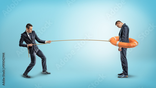 A businessman catches another man with an orange life buoy used as a lasso.