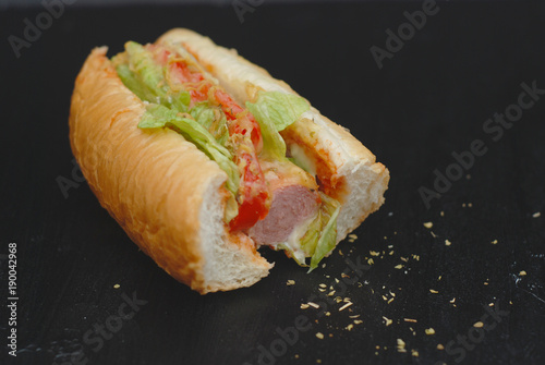 Half Bited Hot Dog on black Board with spices and Letuce, Tomatoes. Healthy Homemade Food. photo