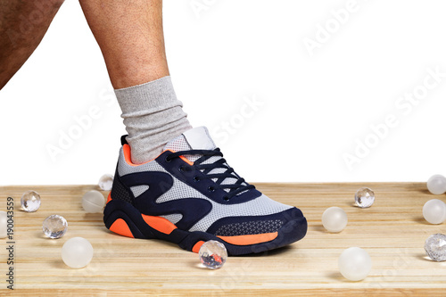 A man s leg  shod in sporting sneakers on a wooden plank floor with a white background