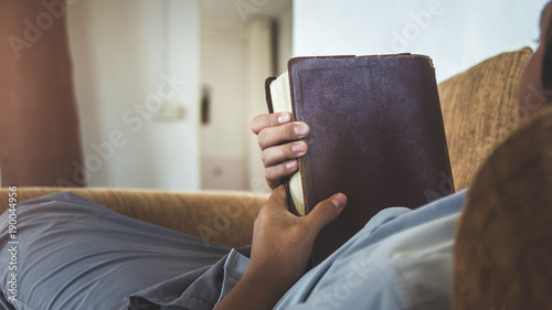 Man holding holy bible on sofa, christian background.